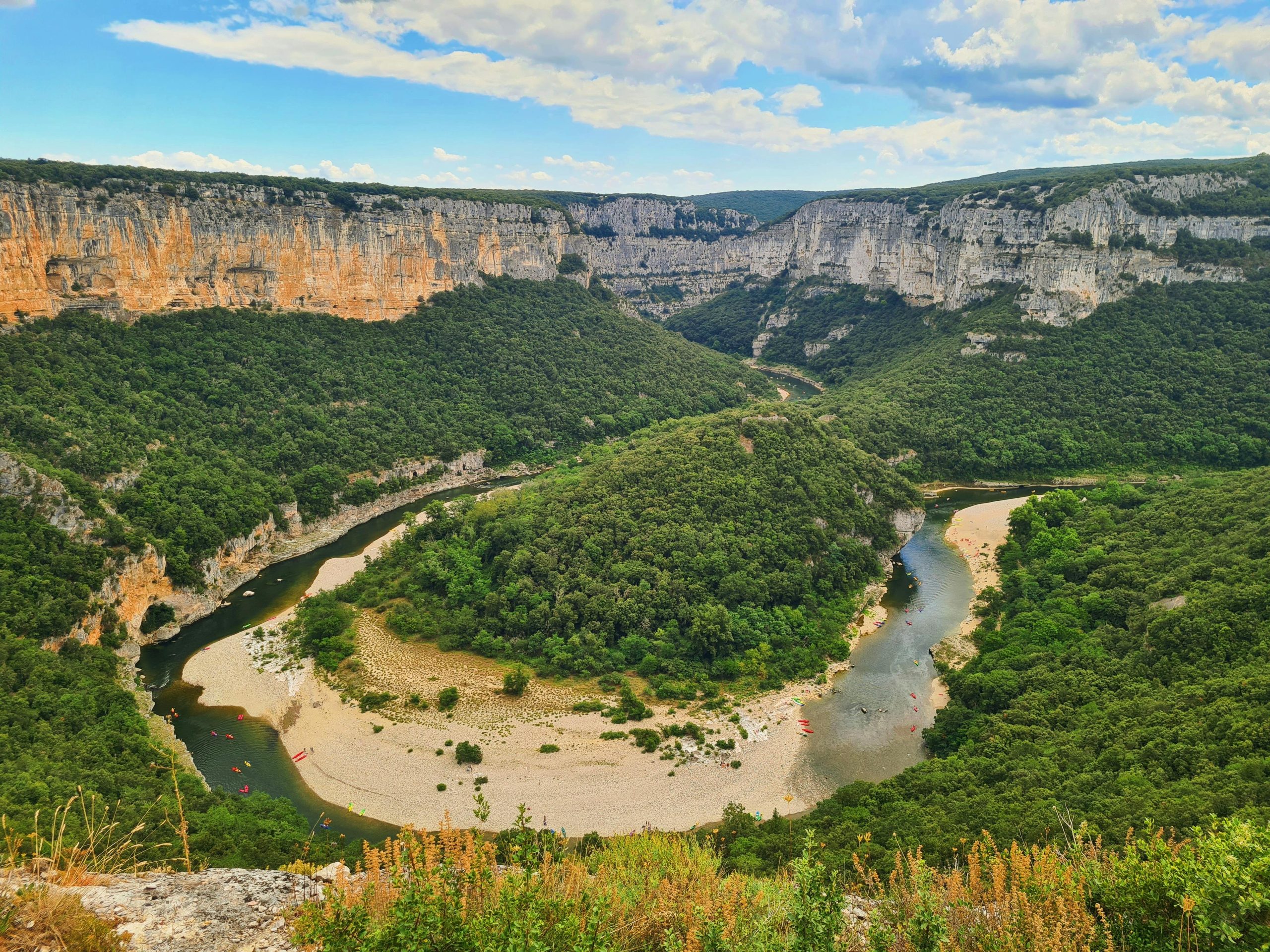 Stunning aerial view of the Ardèche River meandering through lush greenery and limestone cliffs in France.